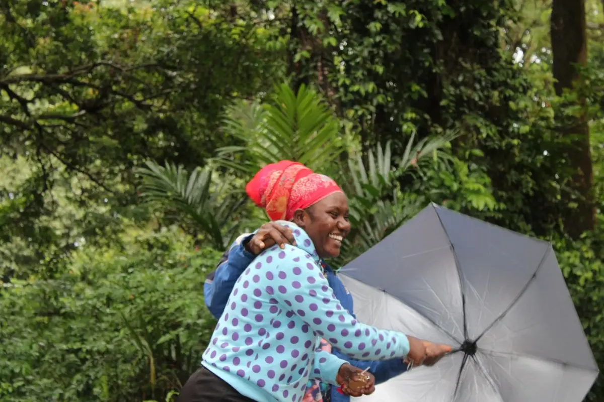 Two visitors laughing together under an umbrella on a leafy forest trail