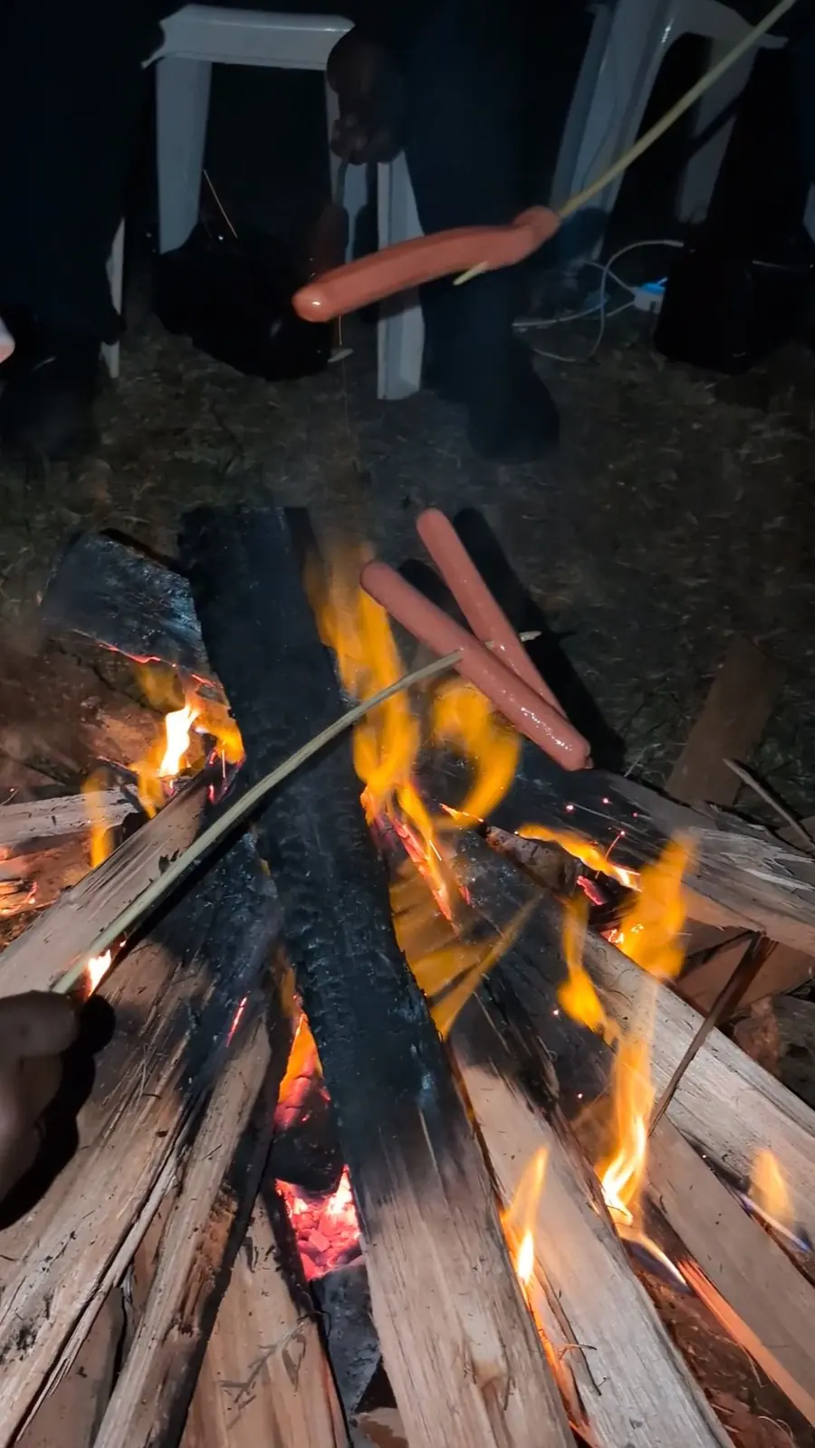 Guests roasting sausages over an evening campfire