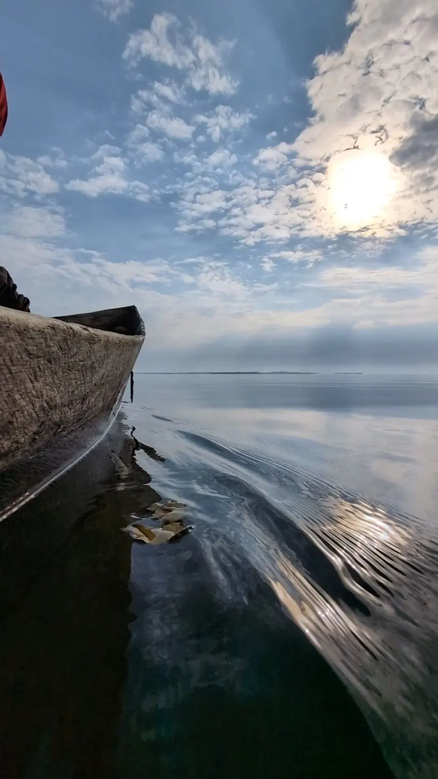 The bow of a wooden canoe gliding across calm water on Lake Nabugabo under a bright sky